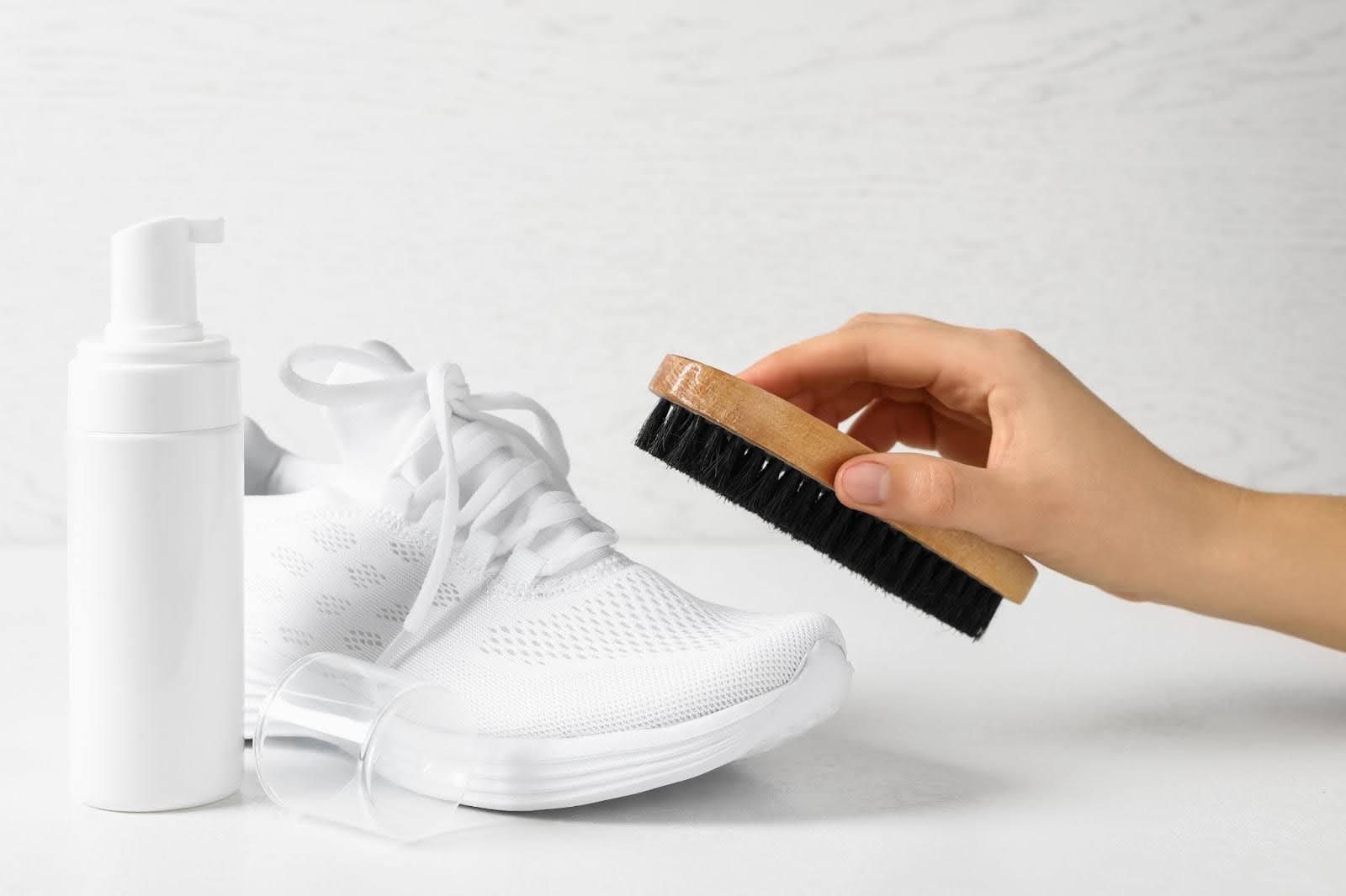 Hand showing how to whiten shoes with brush and cleaner.