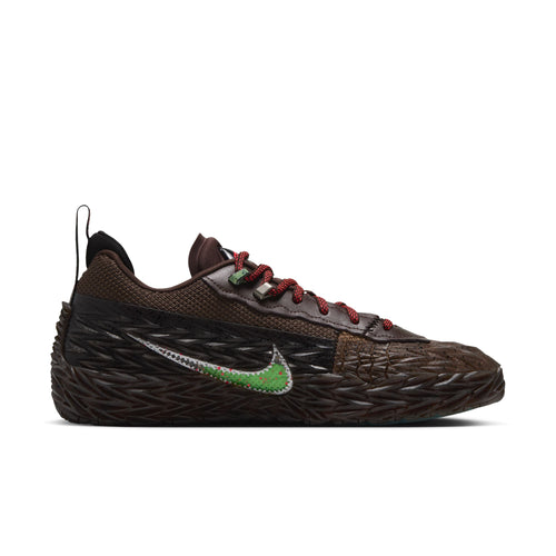 A Nike sneaker in dark brown with a textured, woven-look upper and sole, featuring red laces and a green and silver Swoosh logo on the side, set against a plain white background.