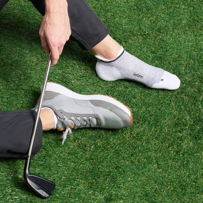 Feetures Elite Golf Max Cushion No Show Tab socks in gray and white with targeted compression and moisture-wicking fabric, worn on golfer.