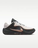 A Nike low top basketball shoe in black and off-white with a metallic rose gold Swoosh, shown in a side profile on a light gray background.