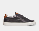 Steve Madden Finneas sneakers in black leather with perforated side panel, brown heel accents, and white rubber outsole, side view.
